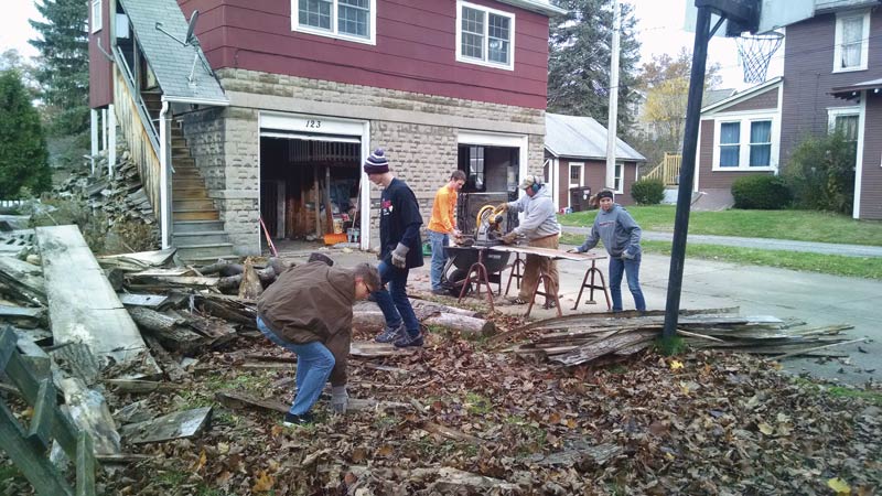 Grove City College (PA) SPS members Seth Byard, Dan Seiter, Connor Murphy, and Mercedes Mansfield help professor Michael Coulter (on the saw) sort and prepare wood for his furnace as part of their Rent-a-Student fundraising campaign in 2015.