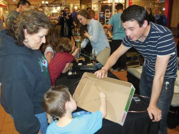  Idaho State University students Justin Anderson  (foreground with the box speaker) and Alexis Chlarson (with the jumping ring demo) engage shoppers at a local mall during an SPS outreach event. Photo courtesy of Steve Shropshire.