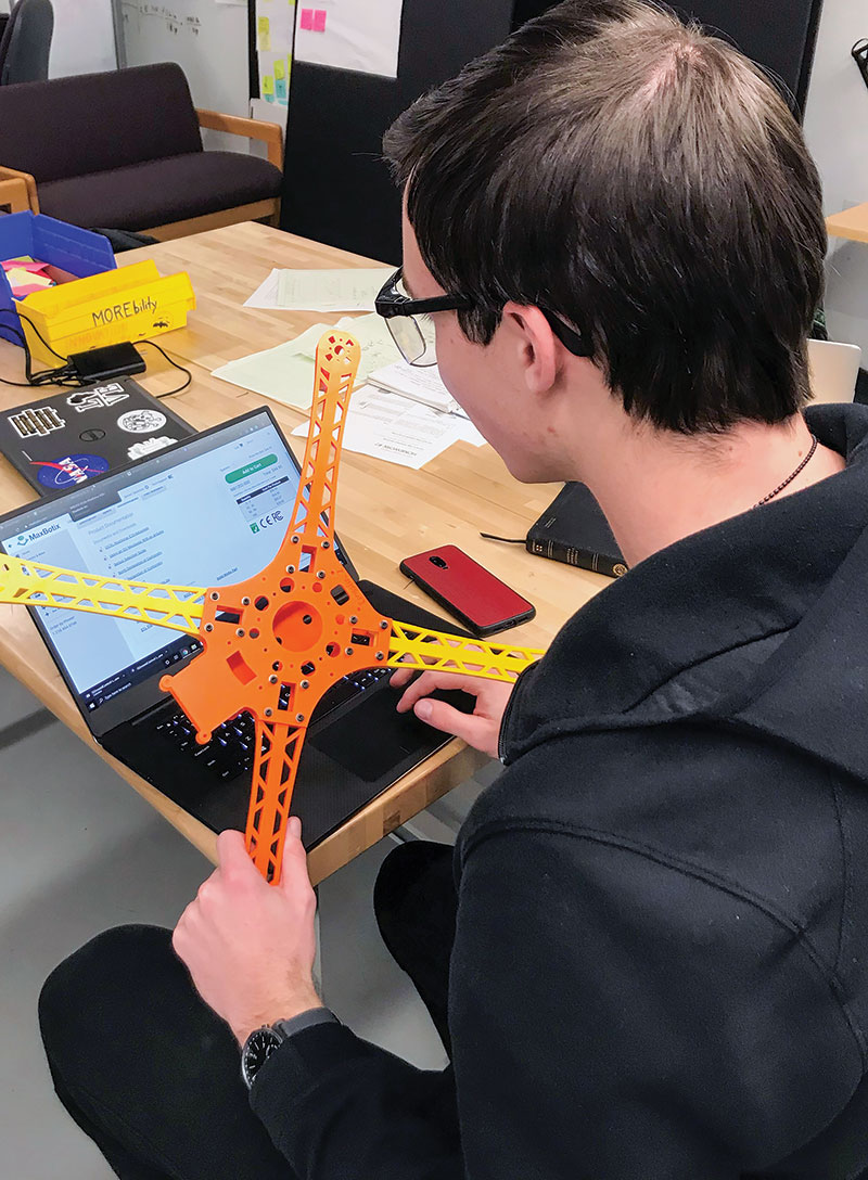 Curtis McLennan, a member of the drone team, holds an assembled 3D-printed drone frame while looking at pricing for sonics sensors. Photo by Sarah Rutt.