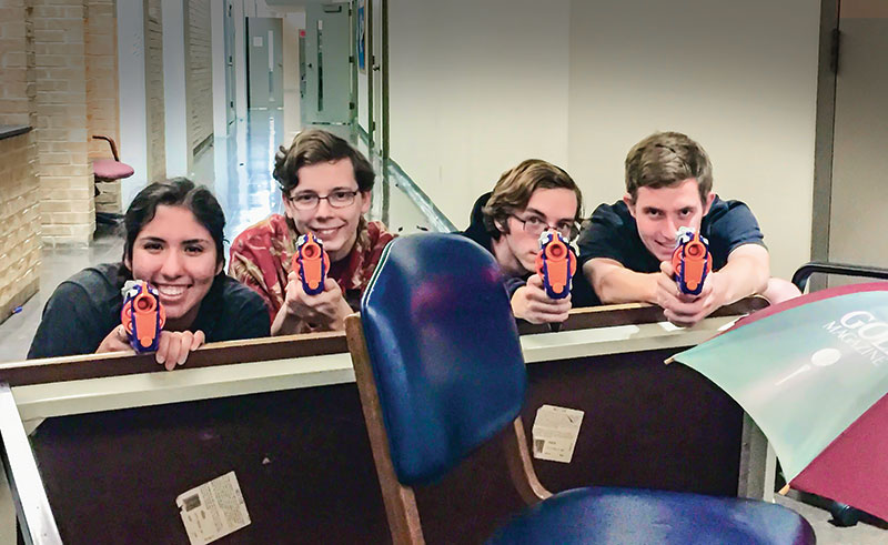 Members of the University of Dallas SPS chapter hiding behind an obstacle made of an overturned table and chair. Photo by Tessa Rosenberger.
